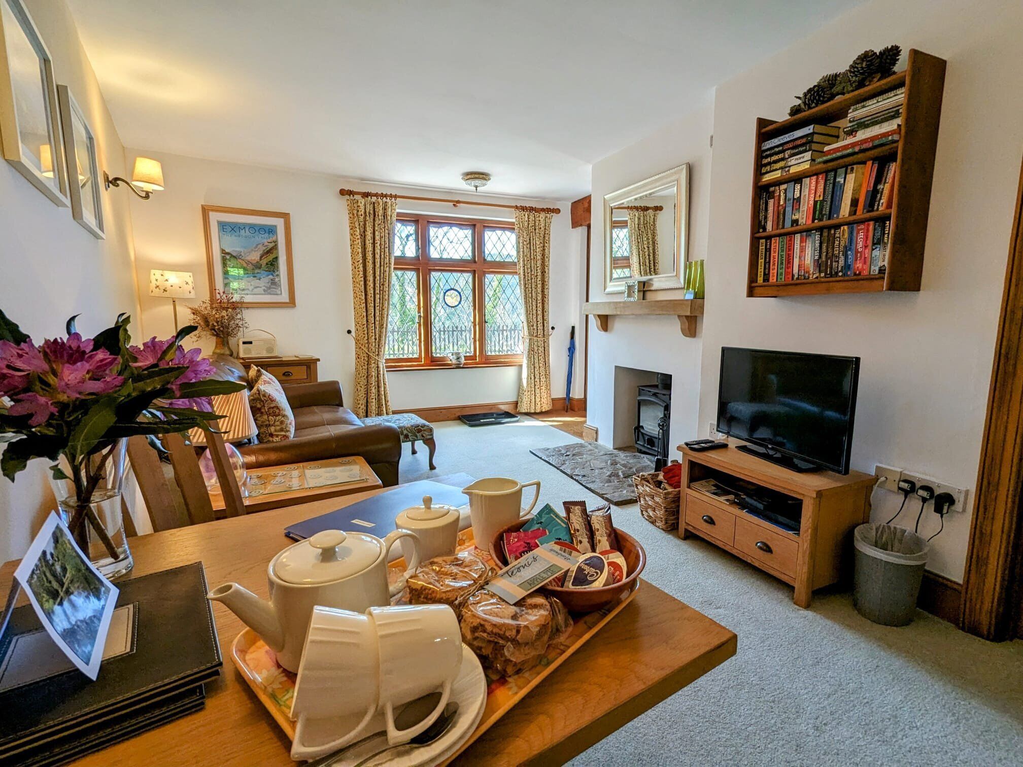 A cozy living room with a fireplace, a television, a bookshelf, and a dining area with a tray of food and drinks.
