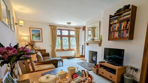 A cozy living room with a fireplace, a television, a bookshelf, and a dining area with a tray of food and drinks. - Gardener Cottage near Martinhoe (Parracombe)