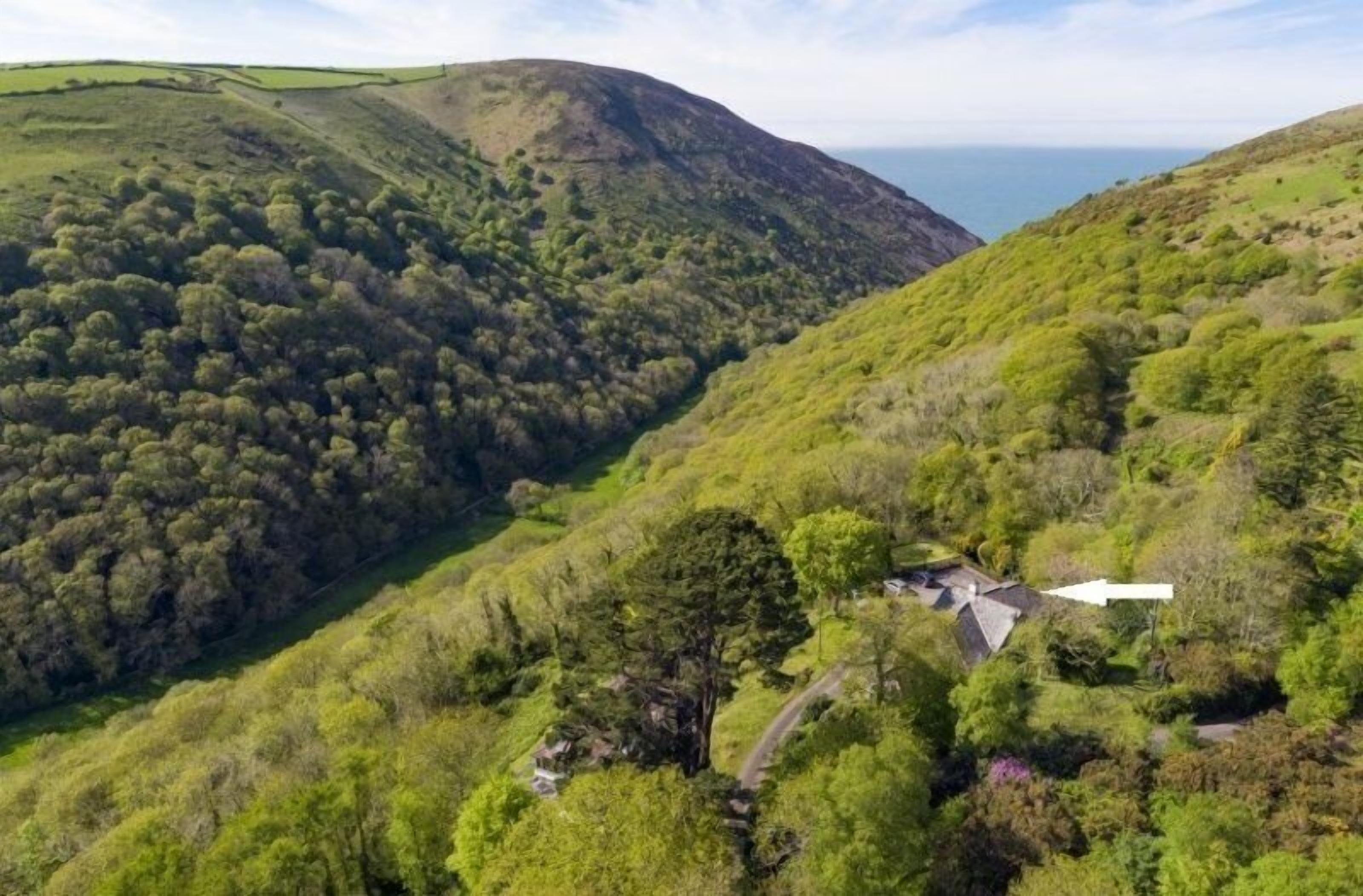 Una valle verdeggiante e isolata, con una piccola casa immersa nella fitta vegetazione e circondata da dolci colline.