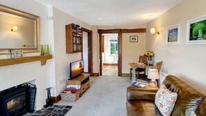 A cozy living room with a fireplace, a leather sofa, a television, and a bookshelf. - Gardener Cottage near Martinhoe (Parracombe)