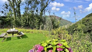 A picnic table with a view of a lush garden and hills in the background. - Gardener Cottage near Martinhoe (Parracombe)