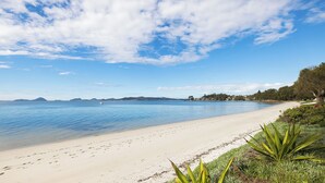 A beach with clear blue water, a sandy shore, and a distant mountain range.