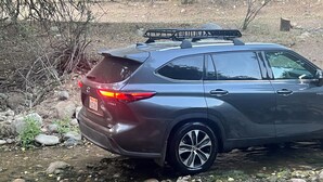 Ein dunkel gefärbtes SUV steht neben einem felsigen Bach.