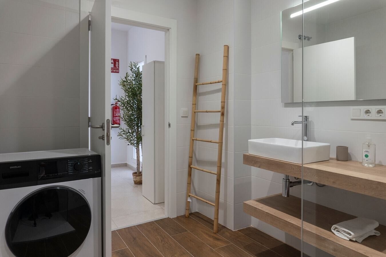 Une salle de bain moderne équipée d’un lave-linge, d’une échelle en bois, d’un évier et d’un miroir.