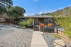 A house with a gravel driveway, a wooden deck with orange cushions, and a mountain backdrop. - Stunning Sequoia Hills Villa w/ pool, Game room, Hot tub, Firepit and EV charger (Three Rivers)