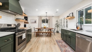 A modern kitchen with a central island, wooden cabinets, and a stainless steel dishwasher. - Stunning Sequoia Hills Villa w/ pool, Game room, Hot tub, Firepit and EV charger (Three Rivers)
