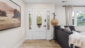 A room with a white door, a framed painting, a grey sofa, and a window with curtains. - Stunning Sequoia Hills Villa w/ pool, Game room, Hot tub, Firepit and EV charger (Three Rivers)