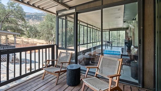 A covered outdoor deck with wicker chairs and a round table, overlooking a pool and a mountainous landscape. - Stunning Sequoia Hills Villa w/ pool, Game room, Hot tub, Firepit and EV charger (Three Rivers)