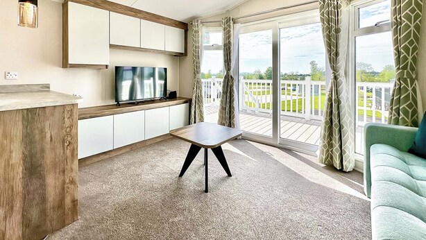 Una cocina moderna con televisor, armarios de madera, una mesa de comedor y un balcón con cortinas.