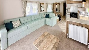Una sala de estar moderna con un sofá modular, una mesa de centro de madera y una zona de cocina con estufa y refrigerador.
