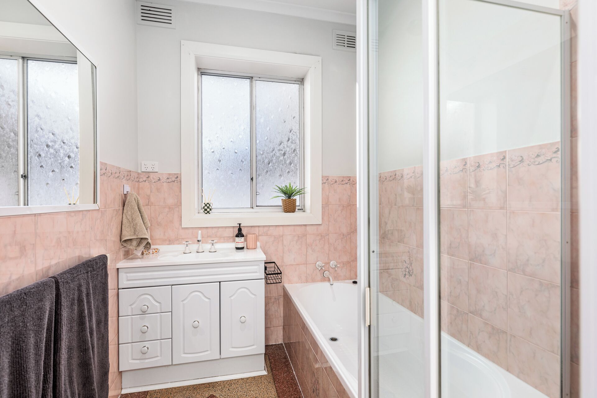 A bathroom with a white vanity, a bathtub, and a window with frosted glass.