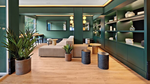 Una sala moderna con sofá, una mesa de centro y plantas en macetas. Se ven estanterías con objetos decorativos y un espejo grande en la pared.