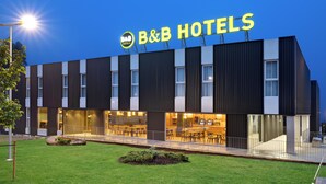 Un moderno hotel tipo B&B con un letrero llamativo, grandes ventanales y un área de estar al aire libre.