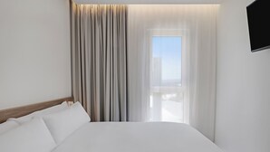 Una habitación de hotel con una cama grande, una ventana con cortinas y un televisor montado.