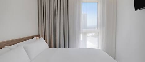 Une chambre d’hôtel avec un grand lit, une fenêtre avec des rideaux et un téléviseur fixé au mur.
