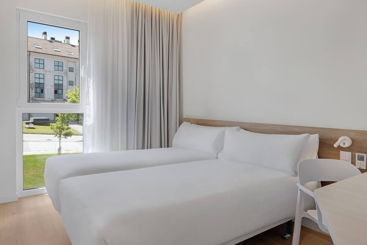 Ein Hotelzimmer mit einem großen Bett, Blick auf ein Gebäude und einem Vorhangfenster.