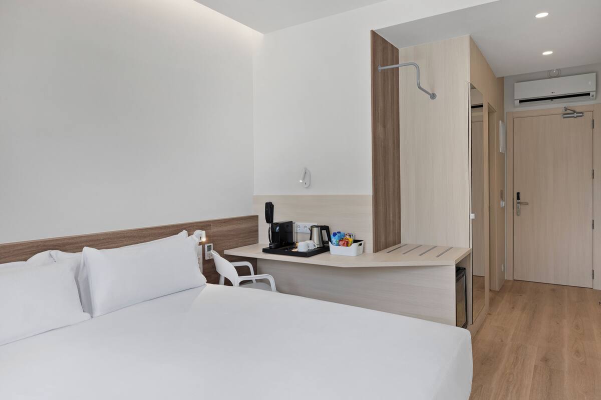 Ein Hotelzimmer mit einem Bett, einem Schreibtisch mit Kaffeemaschine, einem Spiegel und einem Kleiderschrank.