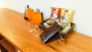 A wooden table with a coffee pot, a glass of orange juice, a wine glass, a wallet, and snack packets. - Hoang Gia Hotel 150 Nghi Tam HN-BayLux (Hanoi)