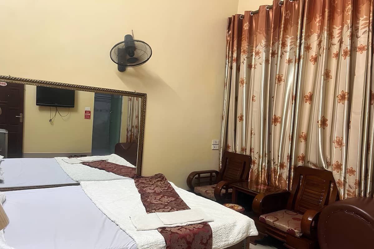 Ein Hotelzimmer mit einem großen Bett, einer Sitzecke mit Sesseln, einem Fernseher und einem Wandventilator.