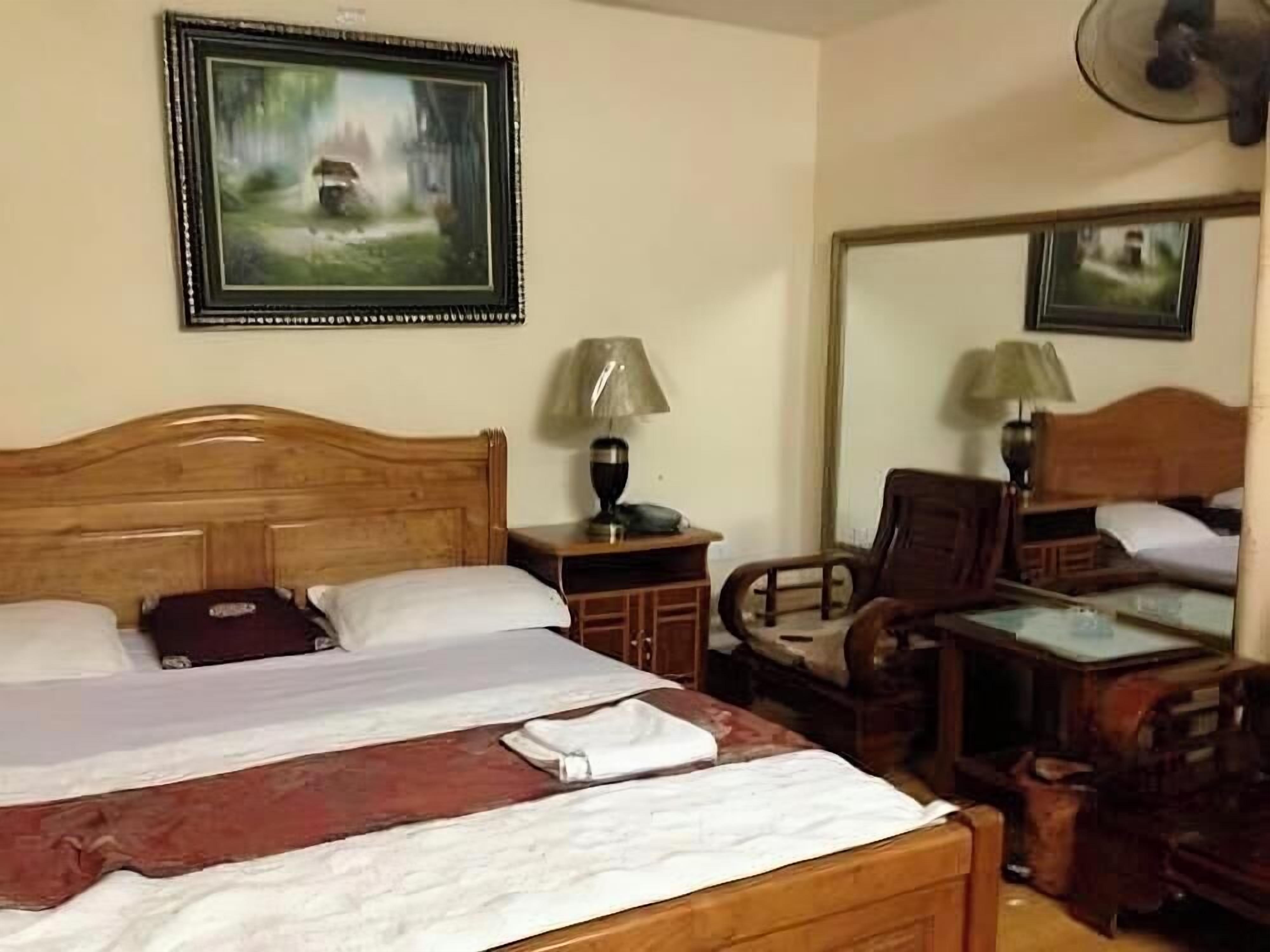 A hotel room with a wooden bed, two bedside tables with lamps, a chair, and a large mirror.