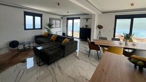 A spacious living area with a sectional sofa, a dining table, and a view of the sea through large windows.