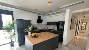 A modern kitchen with a wooden island, dark cabinetry, and a marble floor.
