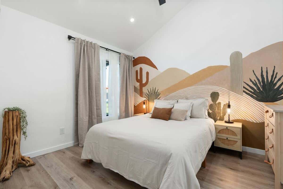 Une chambre à coucher avec un lit, des tables de chevet, un tronc d’arbre en bois et une fresque murale sur le thème du désert.