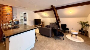 Una cocina moderna con una isla integrada, un área de comedor con sofá y sillas, y una sala de estar con televisor y planta.
