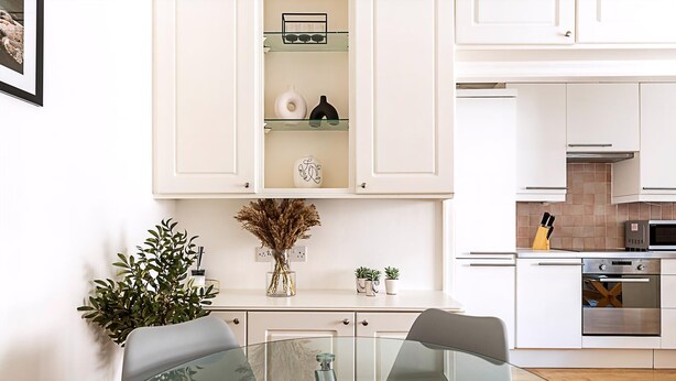 Une cuisine moderne avec des meubles blancs, une table à manger avec un plateau en verre et un four encastré.