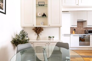 Une cuisine moderne avec des meubles blancs, une table à manger avec un plateau en verre et un four encastré.
