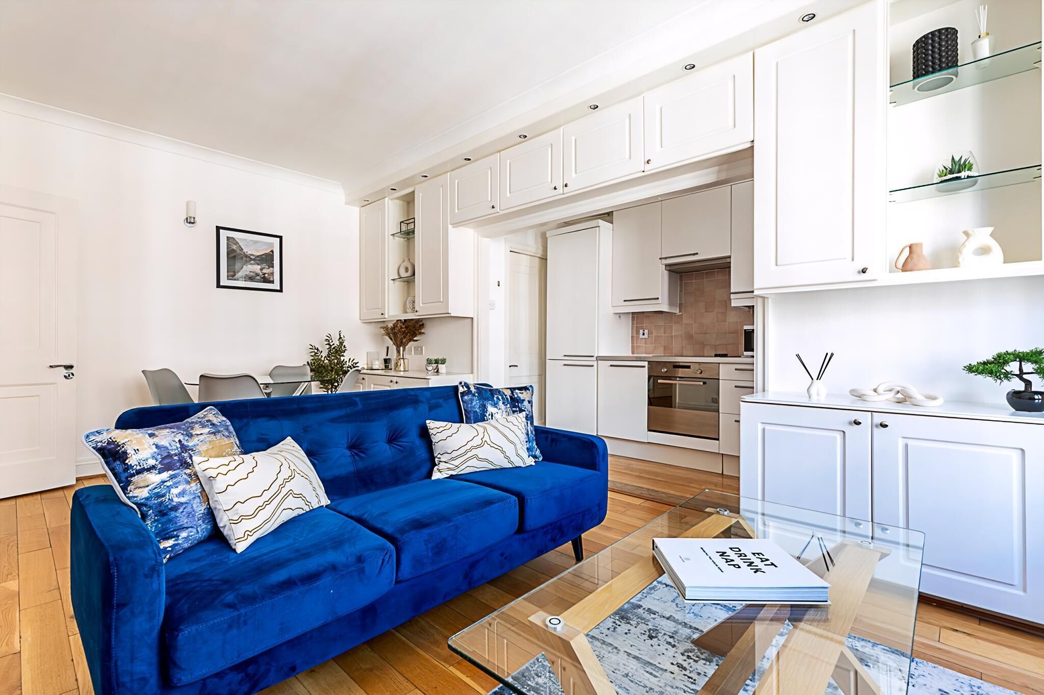 Un salon moderne avec un canapé bleu, une table basse en verre et des meubles blancs.