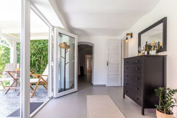 A hallway with a sliding glass door leading to an outdoor seating area, a dark wooden dresser with a mirror, and a potted plant.