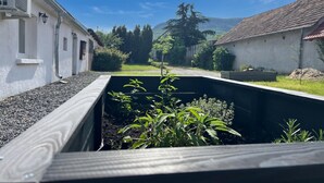 Een plantenbak met beplanting, een wit gebouw met een raam en een rode dakbedekking.