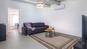 Een moderne woonkamer met een grijze bank, een kamerkleed met patroon, een hanglamp en een kleine ronde tafel met een vaas en een schaal.