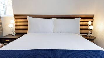 Una cama bien hecha con sábanas blancas y una manta azul, flanqueada por dos mesitas de noche con lámparas.