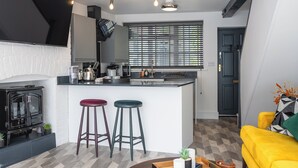A modern kitchen with a central island, bar stools, a stove, and a dining area with a yellow sofa. - Captivating 2-Bed House in Nettleham (Lincoln)