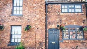 A brick building with a black door, windows, and hanging flower baskets. - Captivating 2-Bed House in Nettleham (Lincoln)