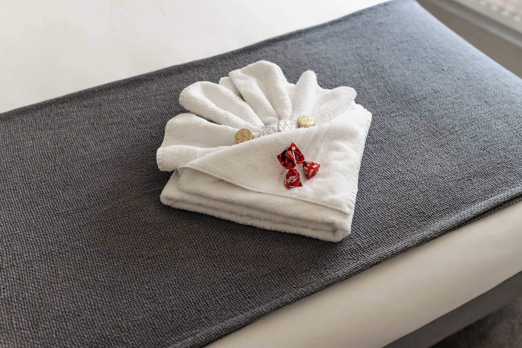 A neatly folded white towel with decorative buttons and a red bow on a grey textured surface.