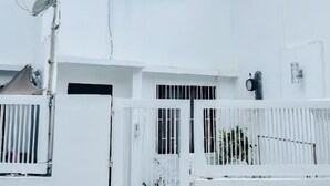 A two-story white building with a gated entrance, satellite dish, and air conditioning units.