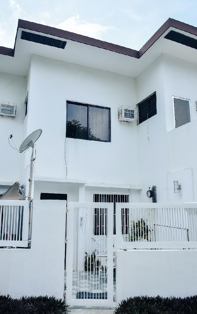 A two-story white building with a gated entrance, satellite dish, and air conditioning units.