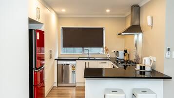 A modern kitchen with a stainless steel refrigerator, a dishwasher, a stove, and a window above the sink.