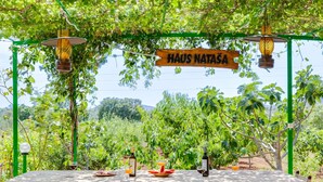 A stone table set outdoors with a sign reading "HAUS NATAŞA" above, surrounded by greenery and trees.