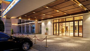 En hotellentrél med en överbyggd gång, en svart bil parkerad framför och en röd avspärrningslina.