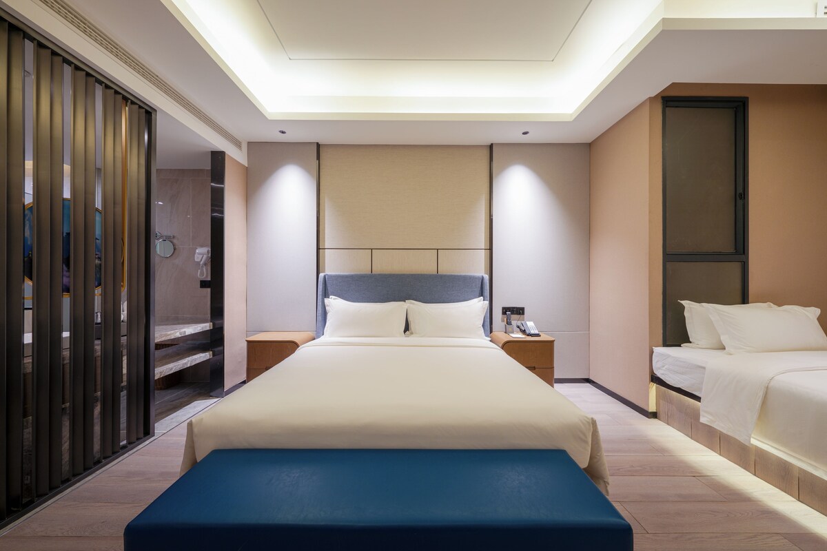 A modern hotel room with a large bed, bedside tables, a bench, and a shower area.