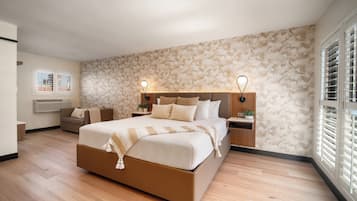 Ein modernes Schlafzimmer mit einem großen Bett, Nachttischen, einem Schreibtischchen und einem Sofa, sowie einem Fenster mit Jalousien.