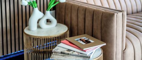 Una sala de estar moderna con un sofá color beige, dos jarrones blancos con flores y una mesita redonda con libros y un álbum de fotos.
