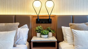 Ein Hotelzimmer mit zwei Betten, einem kleinen Nachttisch aus Holz und einer an der Wand befestigten Leuchte.