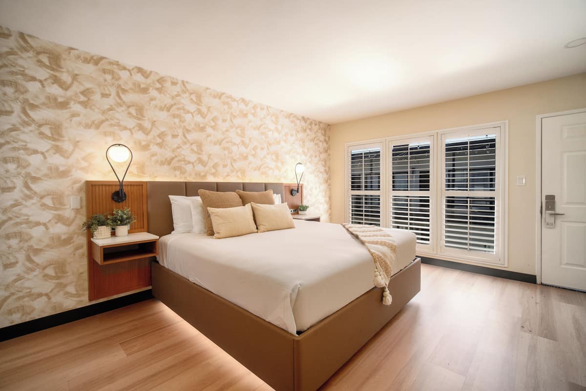 Un dormitorio con una cama grande, suelo de madera, pared estampada y una ventana con persianas.