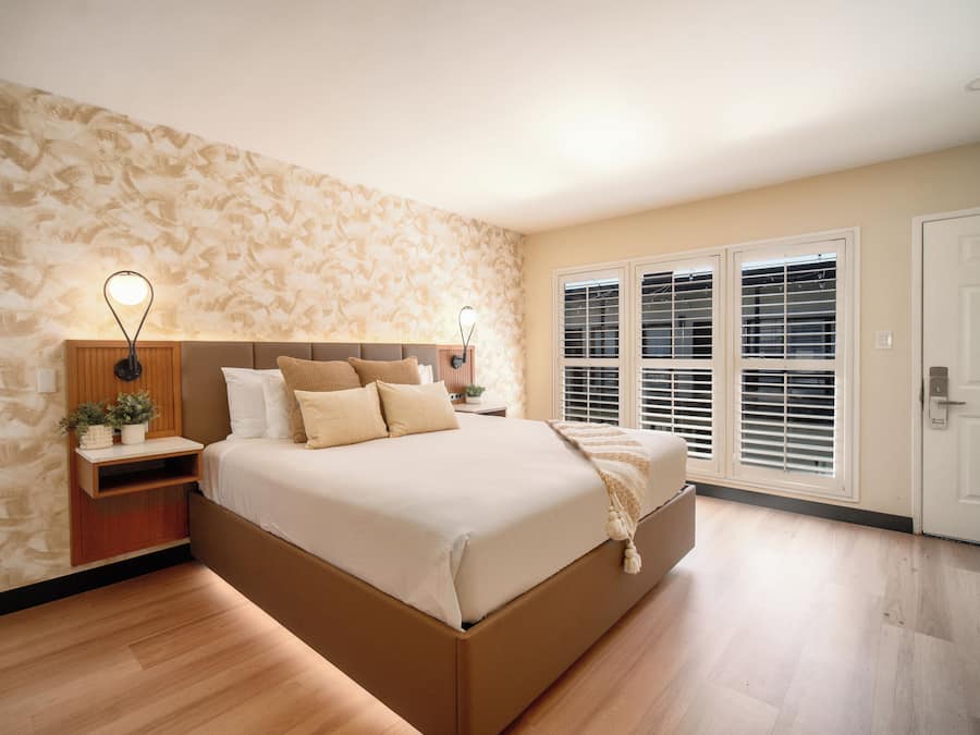 Une chambre avec un grand lit, un plancher en bois, un mur à motifs et une fenêtre avec des stores.