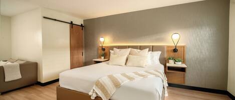Un dormitorio moderno con una cama grande, mesitas de noche con lámparas, un sofá y un armario de madera.
